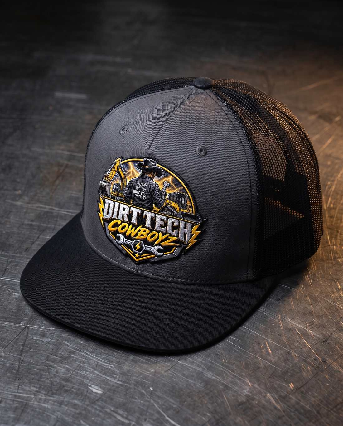 Black and charcoal Dirt Tech Cowboyz trucker cap on a steel workbench.